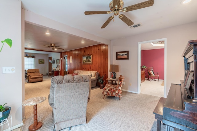 living room with ceiling fan, wooden walls, and light carpet