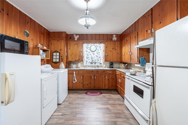 kitchen featuring white appliances, washer and clothes dryer, wooden walls, decorative light fixtures, and hardwood / wood-style floors