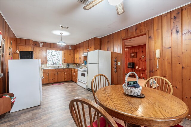 dining space with light hardwood / wood-style flooring, ceiling fan, wooden walls, and crown molding