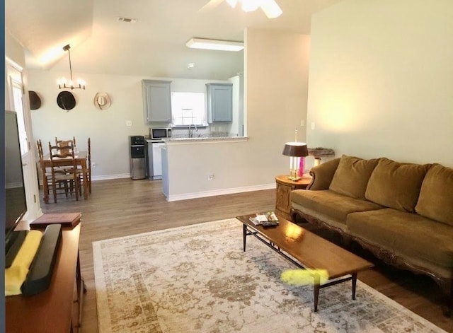 living room featuring ceiling fan with notable chandelier, dark wood-type flooring, and vaulted ceiling