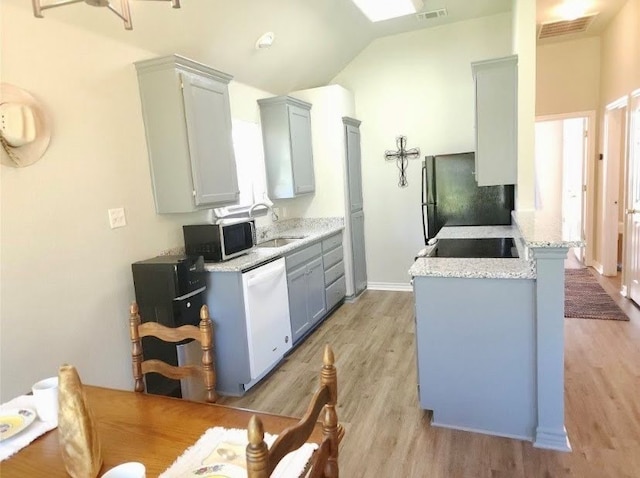 kitchen featuring sink, black fridge, vaulted ceiling, light hardwood / wood-style flooring, and dishwasher