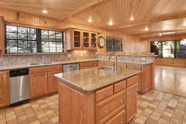 kitchen featuring wood walls, backsplash, sink, stainless steel dishwasher, and an island with sink