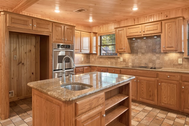 kitchen featuring a center island with sink, light stone counters, and wood walls