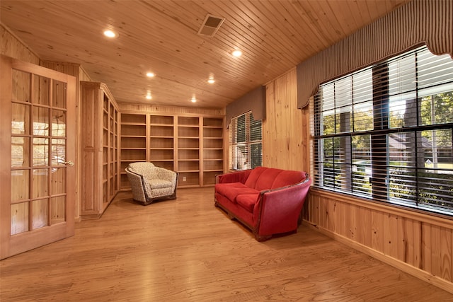 living area featuring a wealth of natural light, light wood-type flooring, wooden walls, and wooden ceiling