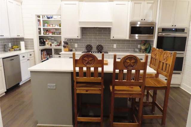 kitchen featuring appliances with stainless steel finishes, dark hardwood / wood-style flooring, premium range hood, a center island, and white cabinetry