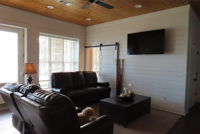 living room featuring ceiling fan, a barn door, wooden ceiling, and wooden walls