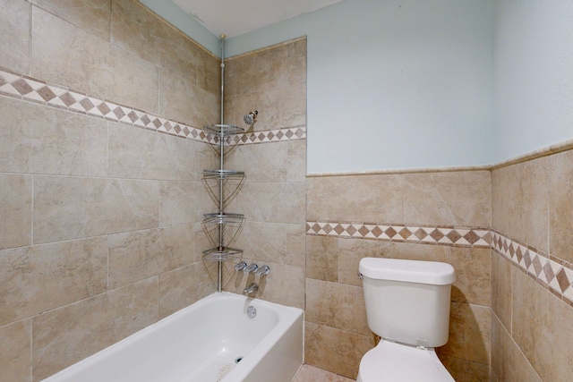 bathroom featuring tiled shower / bath, toilet, and tile walls