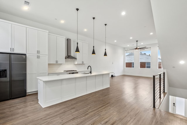 kitchen with decorative light fixtures, an island with sink, white cabinets, stainless steel refrigerator with ice dispenser, and wall chimney exhaust hood