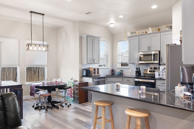 kitchen featuring backsplash, pendant lighting, dark stone counters, light hardwood / wood-style floors, and appliances with stainless steel finishes