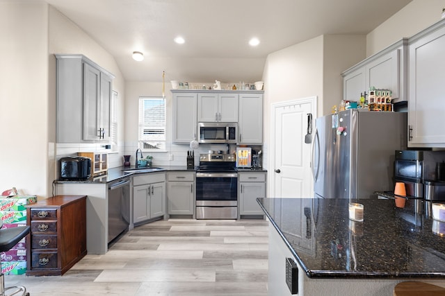 kitchen featuring appliances with stainless steel finishes, backsplash, sink, light hardwood / wood-style flooring, and lofted ceiling