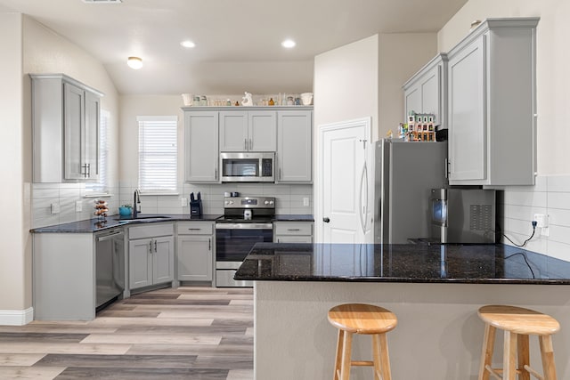 kitchen featuring sink, a breakfast bar area, appliances with stainless steel finishes, kitchen peninsula, and dark stone counters