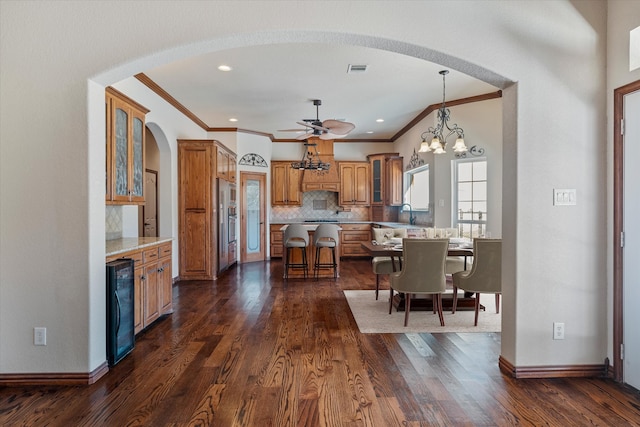 kitchen with a kitchen bar, ceiling fan with notable chandelier, dark wood-type flooring, decorative light fixtures, and a kitchen island