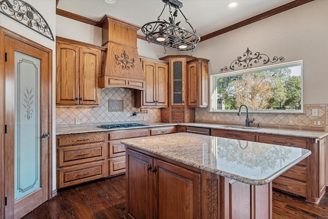 kitchen with sink, ornamental molding, stainless steel gas cooktop, a kitchen island, and decorative light fixtures