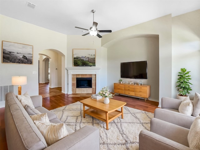 living room with hardwood / wood-style flooring, ceiling fan, and a tiled fireplace