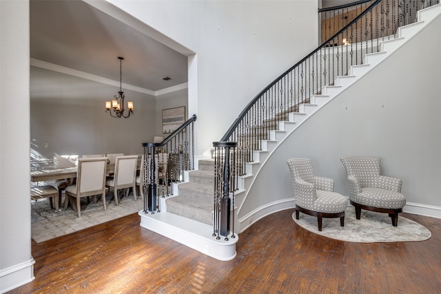 stairs with a chandelier, hardwood / wood-style floors, crown molding, and a high ceiling