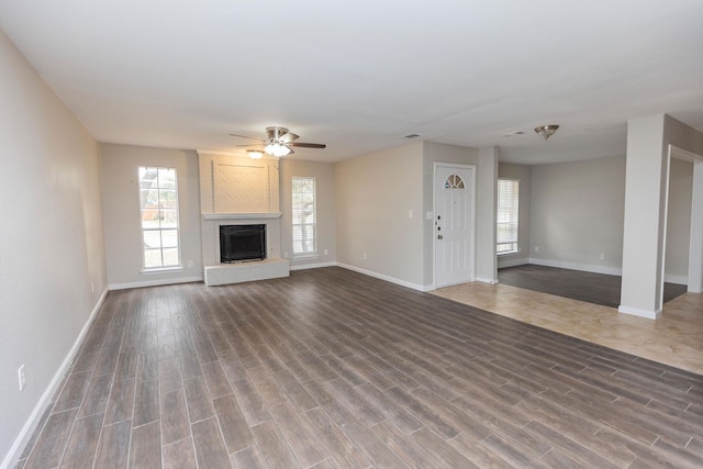 unfurnished living room with a healthy amount of sunlight, a large fireplace, wood-type flooring, and ceiling fan