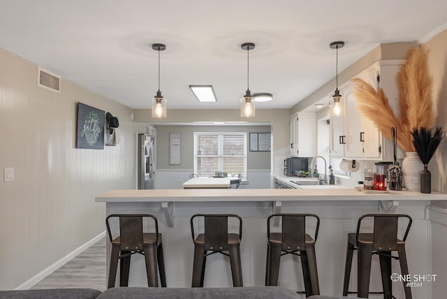 kitchen featuring white cabinets, wood-type flooring, kitchen peninsula, and sink