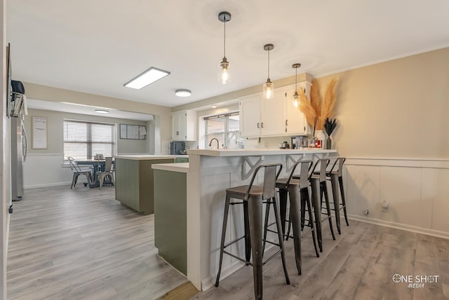 kitchen with white cabinetry, hanging light fixtures, a kitchen breakfast bar, light hardwood / wood-style flooring, and kitchen peninsula