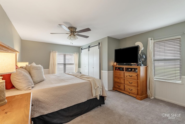 bedroom with ceiling fan, a barn door, and light colored carpet