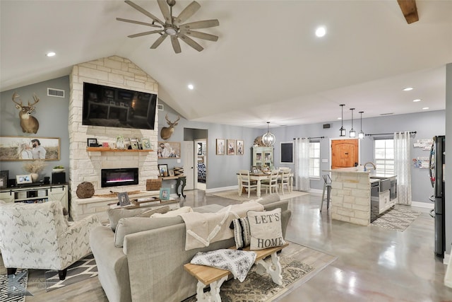 living room featuring ceiling fan, sink, a stone fireplace, and vaulted ceiling