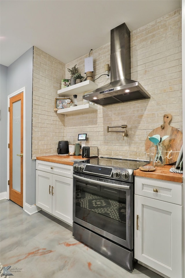 kitchen featuring white cabinetry, wall chimney exhaust hood, brick wall, wooden counters, and stainless steel electric range