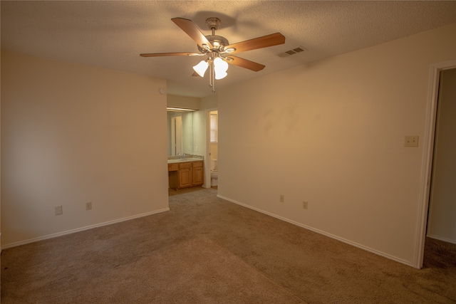 unfurnished bedroom featuring ceiling fan, light colored carpet, a textured ceiling, and ensuite bath