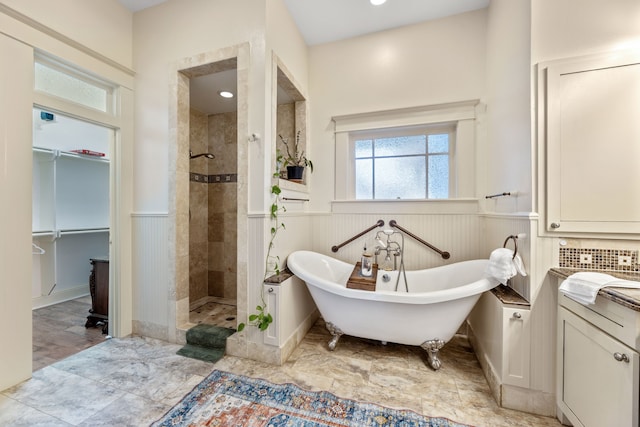 bathroom with a wainscoted wall, a freestanding bath, a spacious closet, and tiled shower