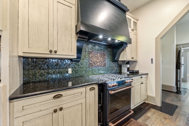 kitchen featuring dark wood-style flooring, tasteful backsplash, premium range hood, stainless steel gas range oven, and baseboards