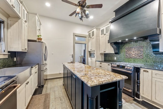 kitchen featuring stainless steel appliances, tasteful backsplash, light wood-style floors, a kitchen island, and wall chimney range hood