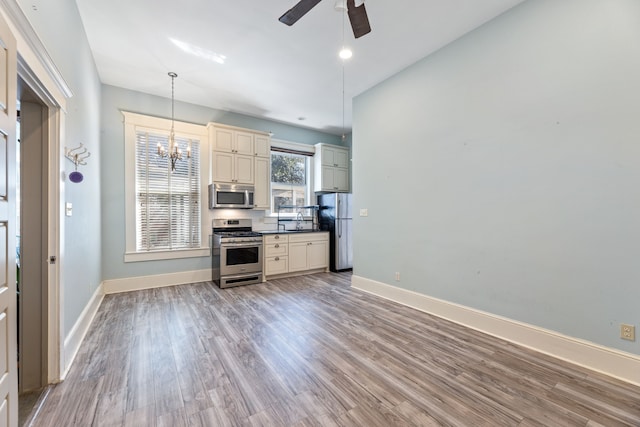 kitchen featuring decorative light fixtures, light wood finished floors, appliances with stainless steel finishes, baseboards, and ceiling fan with notable chandelier