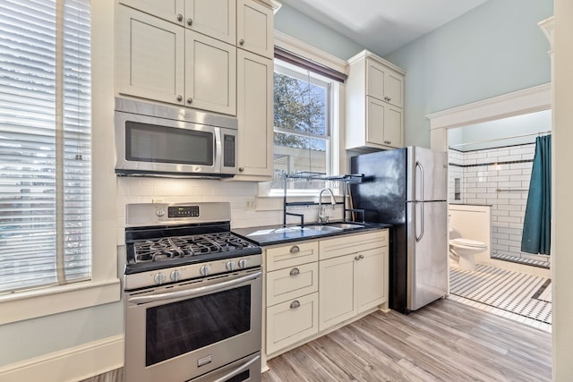 kitchen with light wood-style flooring, a sink, appliances with stainless steel finishes, tasteful backsplash, and dark countertops