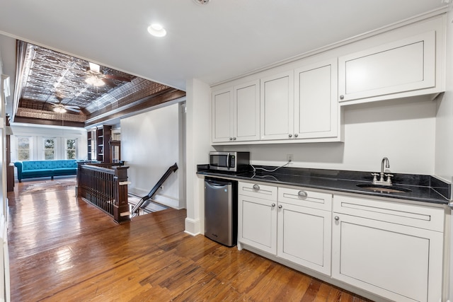 kitchen with a tray ceiling, dark countertops, stainless steel microwave, a sink, and hardwood / wood-style floors