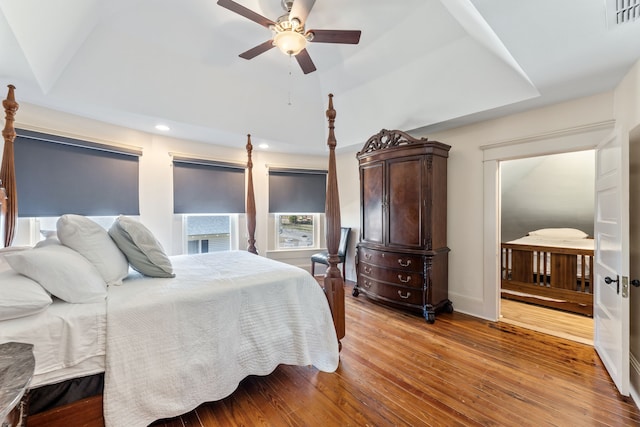 bedroom featuring visible vents, a raised ceiling, baseboards, ceiling fan, and light wood-style flooring