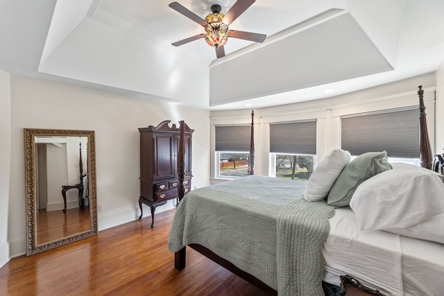 bedroom featuring a raised ceiling, ceiling fan, baseboards, and wood finished floors