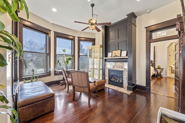 living area with arched walkways, a premium fireplace, ceiling fan, baseboards, and hardwood / wood-style flooring