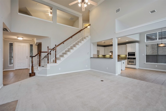 unfurnished living room with a towering ceiling, light colored carpet, ceiling fan, and ornamental molding