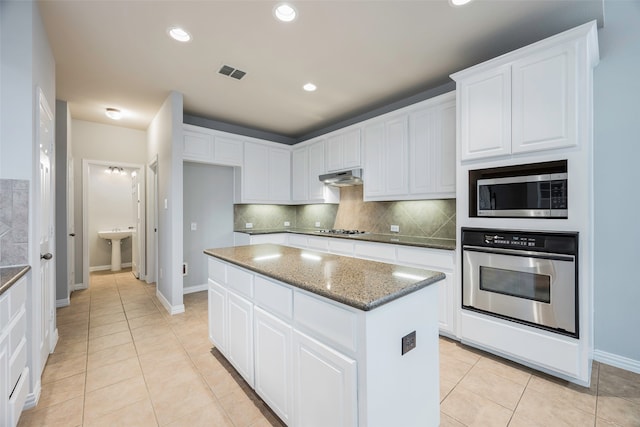 kitchen with appliances with stainless steel finishes, dark stone counters, a kitchen island, white cabinetry, and light tile patterned flooring