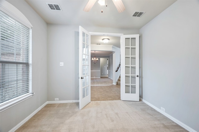 spare room with light carpet, french doors, ceiling fan with notable chandelier, and plenty of natural light