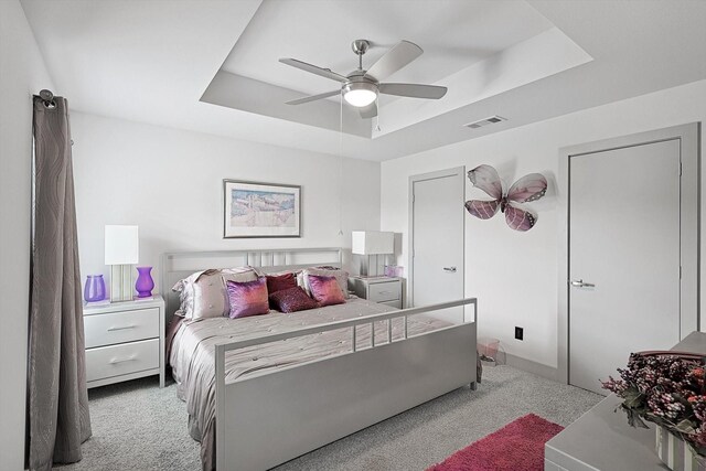 carpeted bedroom featuring a tray ceiling and ceiling fan