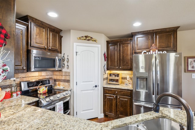 kitchen featuring light stone countertops, dark brown cabinets, backsplash, and stainless steel appliances