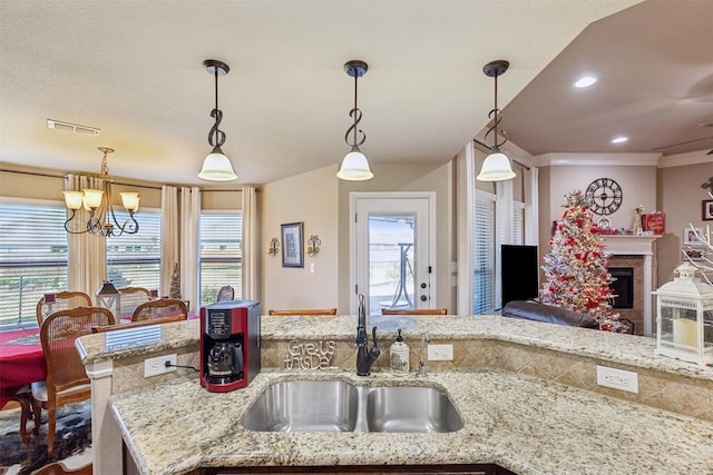 kitchen featuring light stone countertops, sink, an inviting chandelier, crown molding, and decorative light fixtures