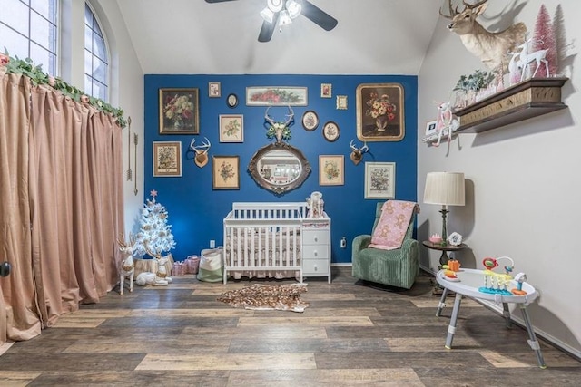 bedroom with a crib, ceiling fan, dark hardwood / wood-style floors, and vaulted ceiling