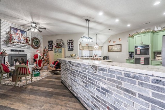 kitchen with stainless steel double oven, dark wood-type flooring, a fireplace, hanging light fixtures, and green cabinets