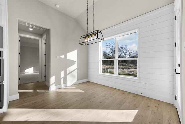 unfurnished dining area with light wood-type flooring, vaulted ceiling, a healthy amount of sunlight, and wood walls