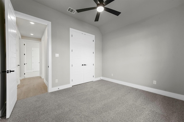 unfurnished bedroom featuring ceiling fan, a closet, light colored carpet, and vaulted ceiling