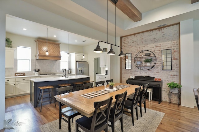 dining area with brick wall, beam ceiling, and light hardwood / wood-style flooring