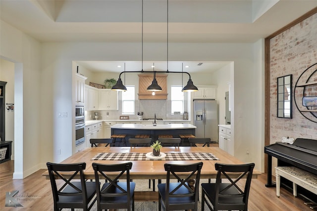 kitchen with appliances with stainless steel finishes, white cabinetry, hanging light fixtures, an island with sink, and brick wall