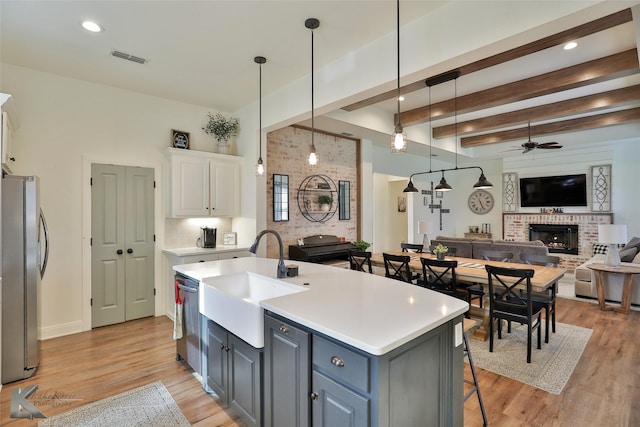 kitchen with sink, a center island with sink, appliances with stainless steel finishes, a fireplace, and white cabinets