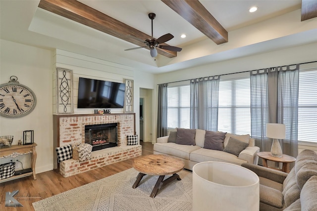 living room with hardwood / wood-style floors, a fireplace, beamed ceiling, and ceiling fan