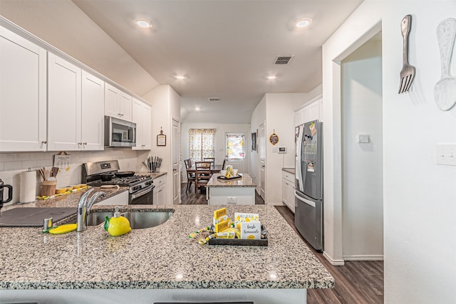 kitchen with white cabinets, stainless steel appliances, light stone counters, and dark wood-type flooring